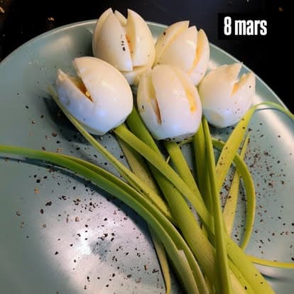 An edible bouquet of white tulips carved from hard-boiled eggs, with spring onion and leek-green stems on a plate; the original photograph includes the inscription “8 mars”.